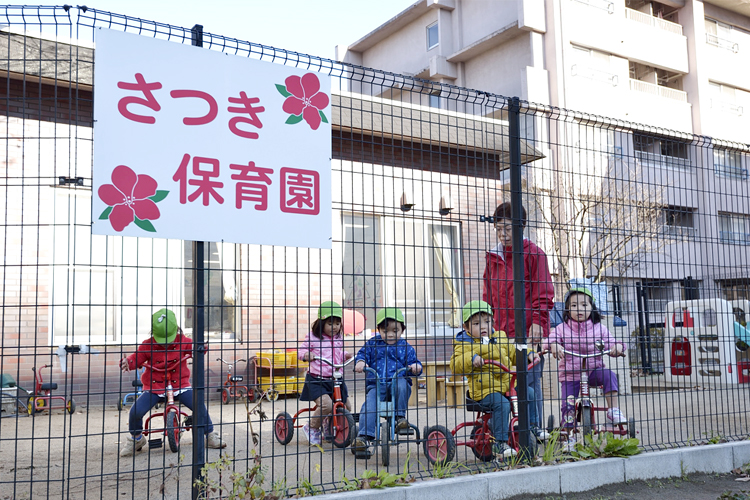 写真：保育園の庭で三輪車に乗る子供たち