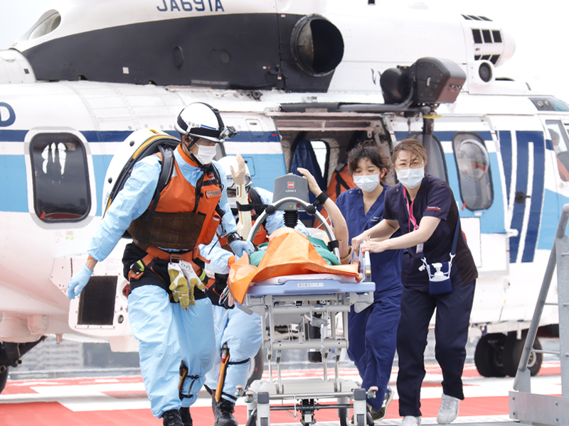 写真:ヘリからストレッチャーで傷病者を運ぶ特殊救難隊員と当院スタッフ