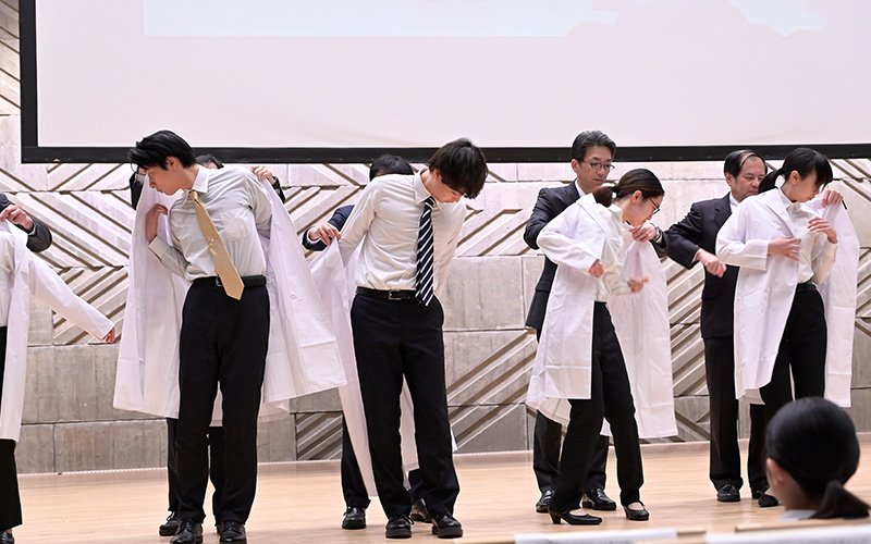 画像:保護者らに見守られる中、教授らに白衣を着せかけられる学生たち