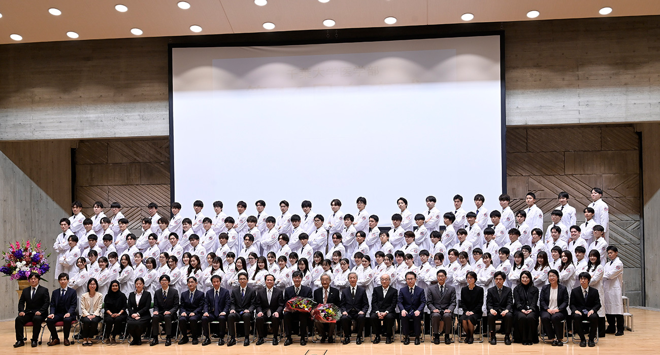 画像：千葉医学のマーク(※ 獅胆鷹目行以女手)のワッペンが付けられた真新しい白衣を着た115名の学生たち