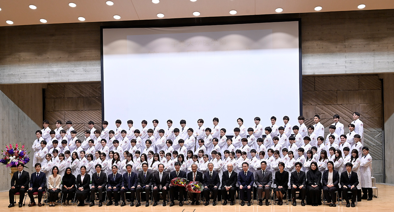 画像:千葉医学のマーク(※ 獅胆鷹目行以女手)のワッペンが付けられた真新しい白衣を着た115名の学生たち